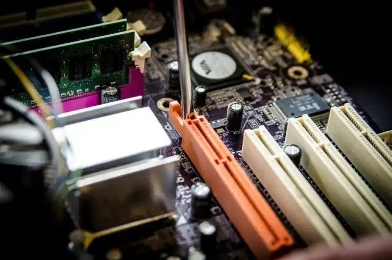 Close-up of screwdriver inserting into PC motherboard slot amid RAM and components for expert computer repair.